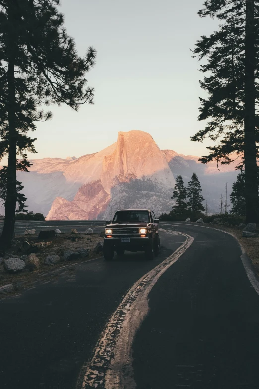 a truck driving down a road with a mountain in the background, a picture, unsplash contest winner, hudson river school, yosemite, 🚿🗝📝, filtered evening light, profile picture