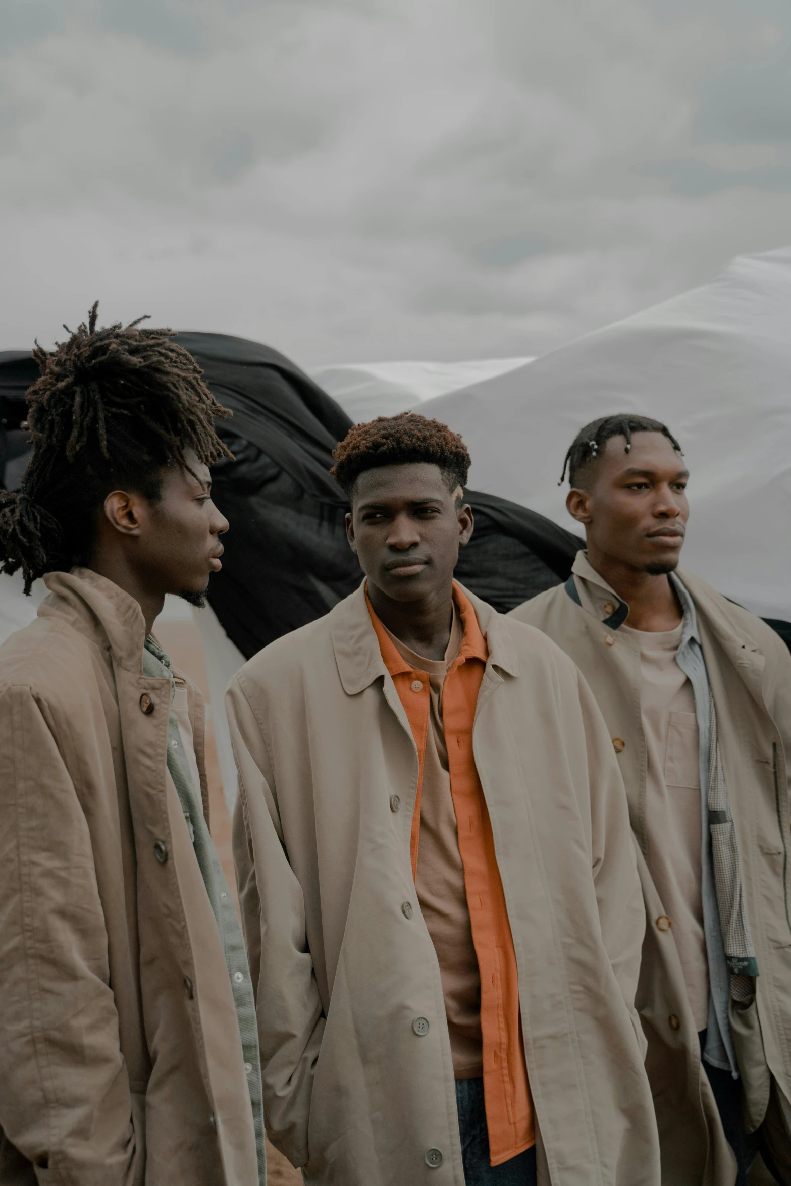 a group of men standing next to each other, trending on unsplash, afrofuturism, brown clothes, ( ( theatrical ) ), overcast, looking away