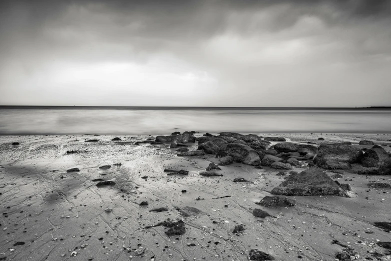 a black and white photo of a beach, a black and white photo, by Andrew Bell, grey skies, wet rocks, medium format, mixed art