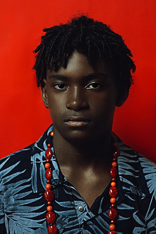 a man standing in front of a red wall, by Lily Delissa Joseph, pexels contest winner, afrofuturism, portrait of 14 years old boy, neck chains, dark blue and red, promotional image