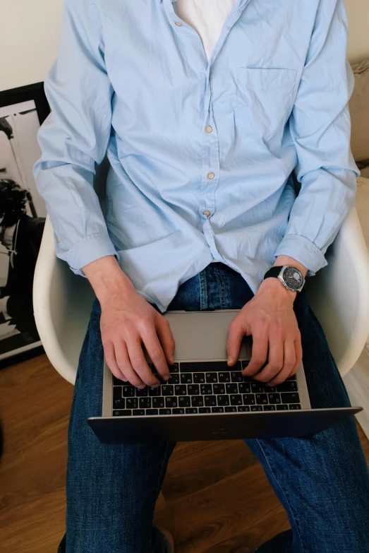 a man sitting in a chair with a laptop, by Carey Morris, pexels, wearing a light blue shirt, holding arms on holsters, programmer, wearing elegant casual clothes