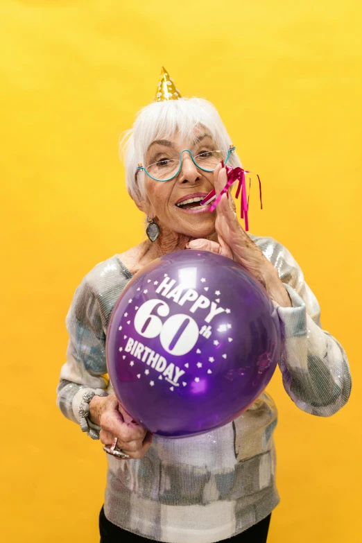 a woman holding a purple balloon with the number 60 on it, by Jeka Kemp, pexels contest winner, old lady screaming and laughing, holding a birthday cake, betty la fea, silver and yellow color scheme