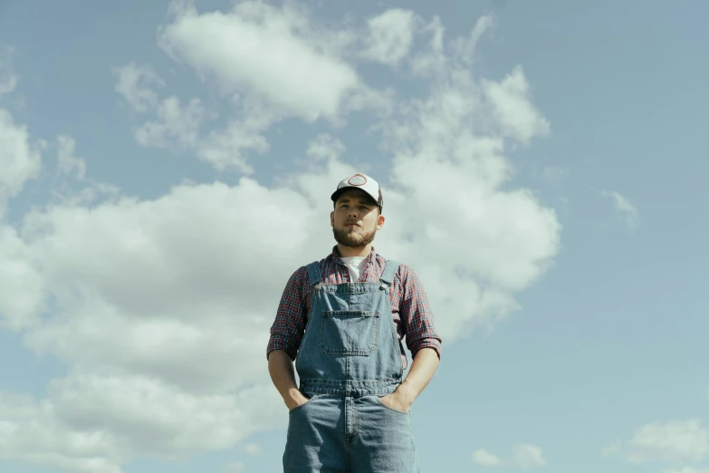 a man standing on top of a lush green field, a portrait, by Mike Bierek, wearing blue jean overalls, uniform off - white sky, profile image, wearing farm clothes