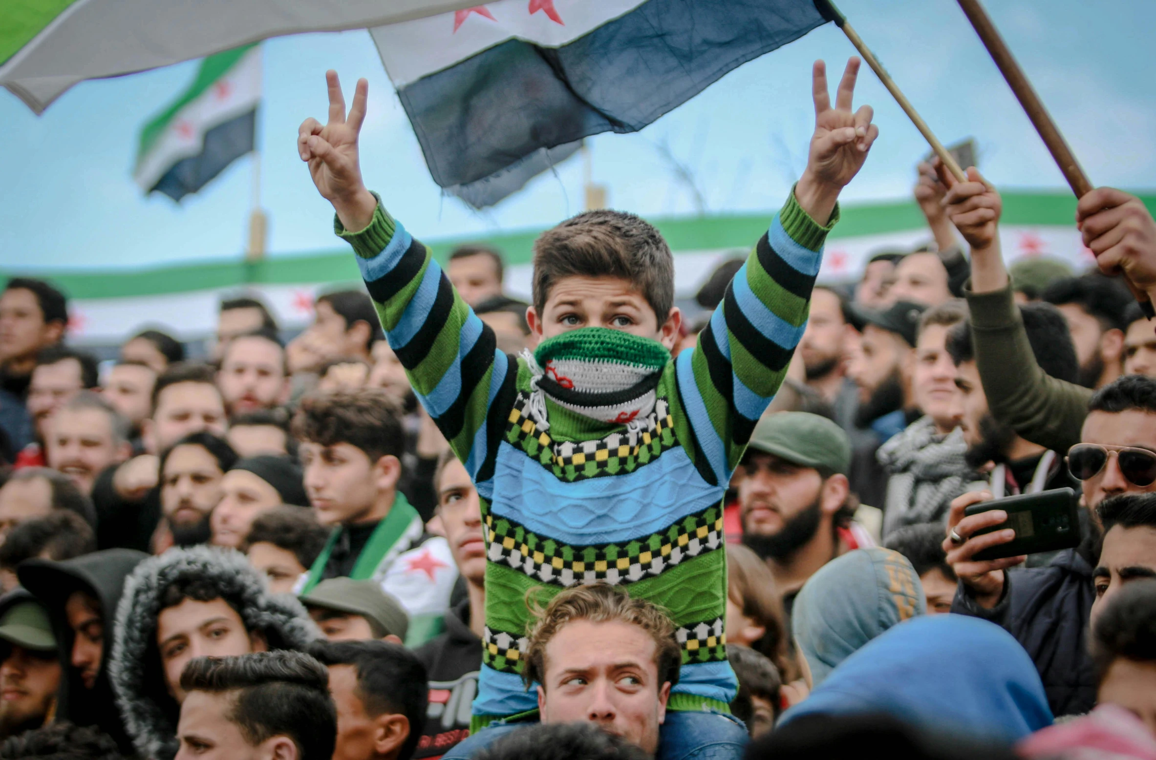 a man holding a flag in front of a crowd of people, shutterstock, hurufiyya, holding his hands up to his face, green and black colors, boys, square