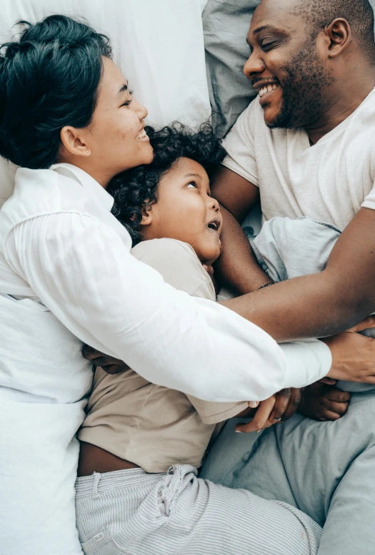 a man and woman laying in bed with a child, pexels contest winner, incoherents, hugging each other, african american, clean design, medium closeup shot