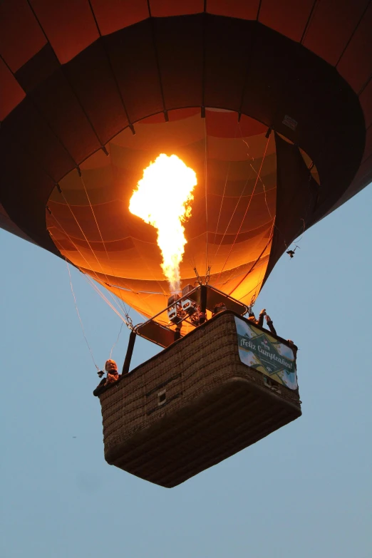 a hot air balloon that is flying in the sky, large flames, in the sun