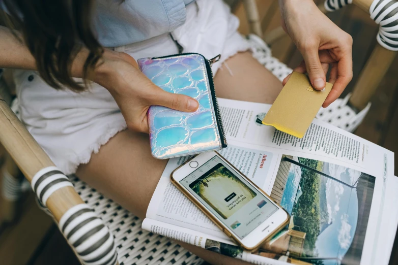 a woman sitting on a chair holding a cell phone, a picture, by Julia Pishtar, trending on pexels, pouches, white holographic plastic, flatlay book collection, poolside