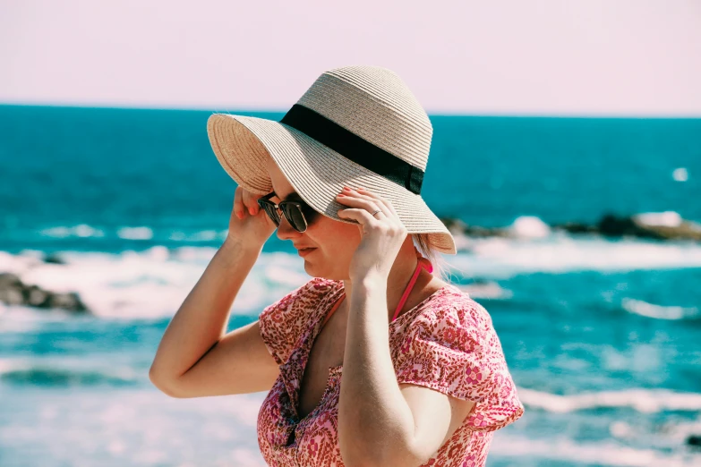 a woman standing on top of a beach next to the ocean, wearing sunglasses and a hat, pink, zoomed in, avatar image