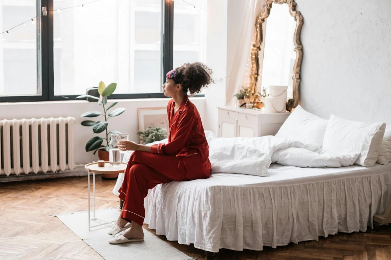 a woman sitting on top of a bed next to a window, trending on pexels, red suit, with a mirror, someone in home sits in bed, on a white table