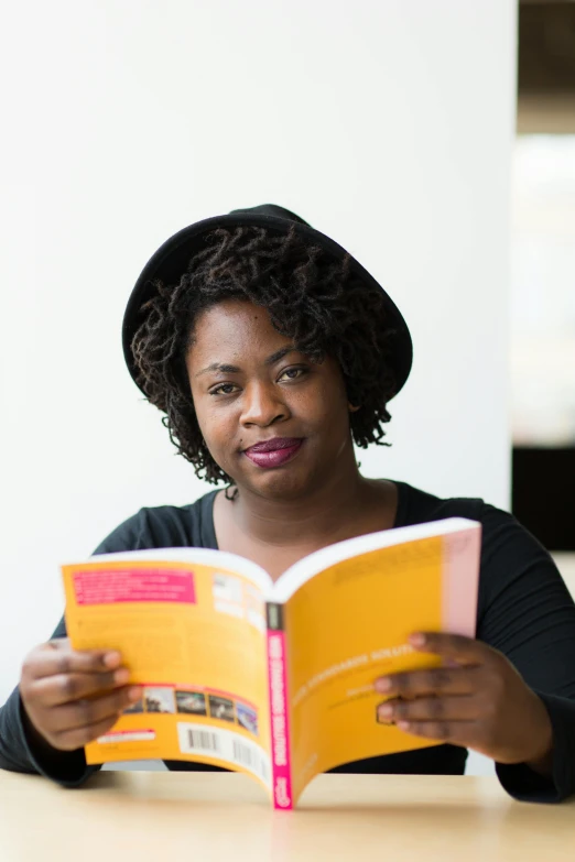 a woman sitting at a table reading a book, by Lily Delissa Joseph, happening, on a yellow paper, headshot, emmanuel shiru, high resolution photo