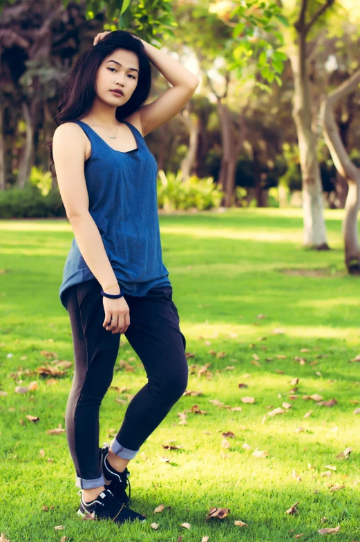 a woman standing on top of a lush green field, wearing : tanktop, blue pants, blue-black, leggings