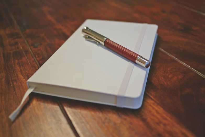 a pen sitting on top of a notebook on a wooden table, white finish, thumbnail, mundane, rectangular