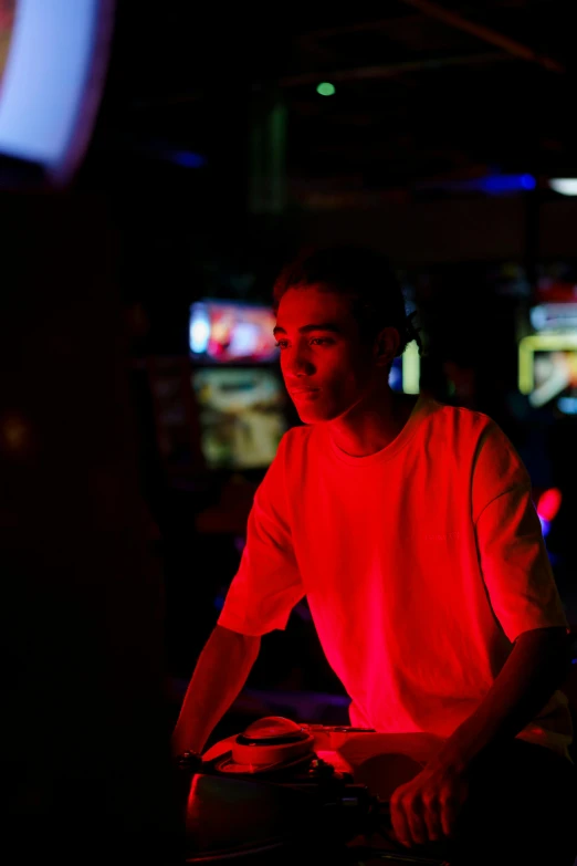 a man playing a video game in a dark room, sitting at a bar, light stubble with red shirt, asher duran, arcade cabinet