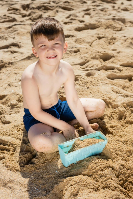 a young boy playing in the sand at the beach, square, blue shorts, box, bio-inspired