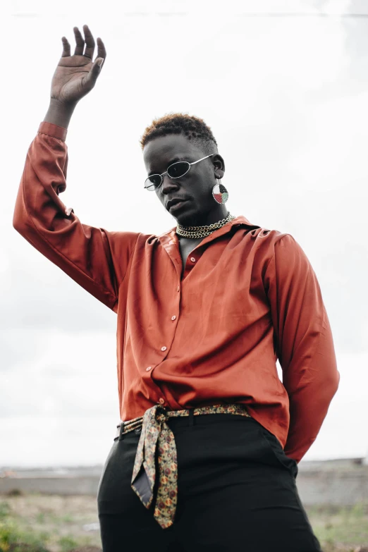 a man in a red shirt and black pants, an album cover, inspired by David Bailly, trending on pexels, grey skinned, samburu, pose model, wearing gold glasses