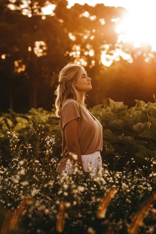 a woman standing in a field at sunset, by Jesper Knudsen, happening, lush surroundings, blonde women, sun beaming down on him, 2019 trending photo