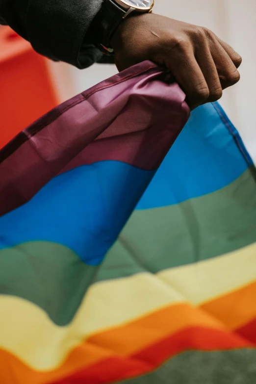 a close up of a person holding a rainbow flag, by Arabella Rankin, trending on unsplash, brown, 🚿🗝📝
