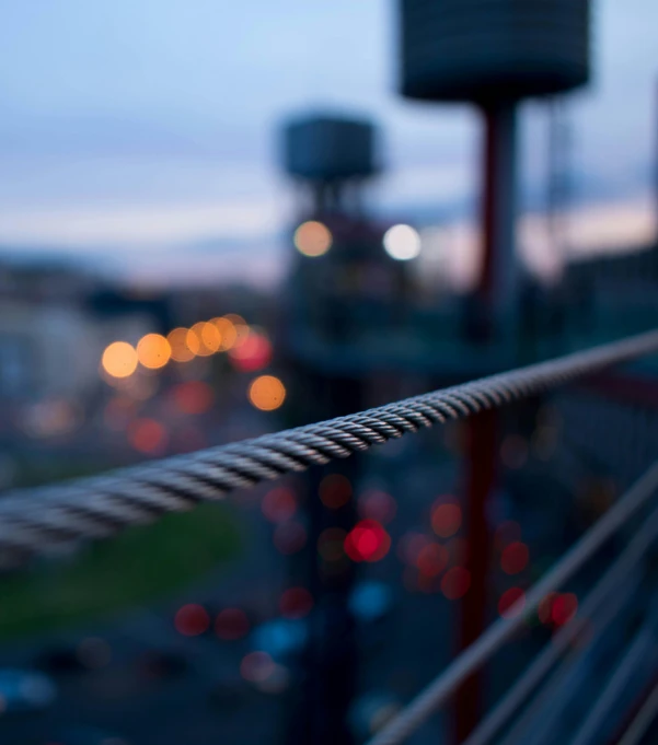 a close up of a wire with a city in the background, by Mathias Kollros, pexels contest winner, happening, evening lights, railing, shallow depth of fielf, today\'s featured photograph 4k