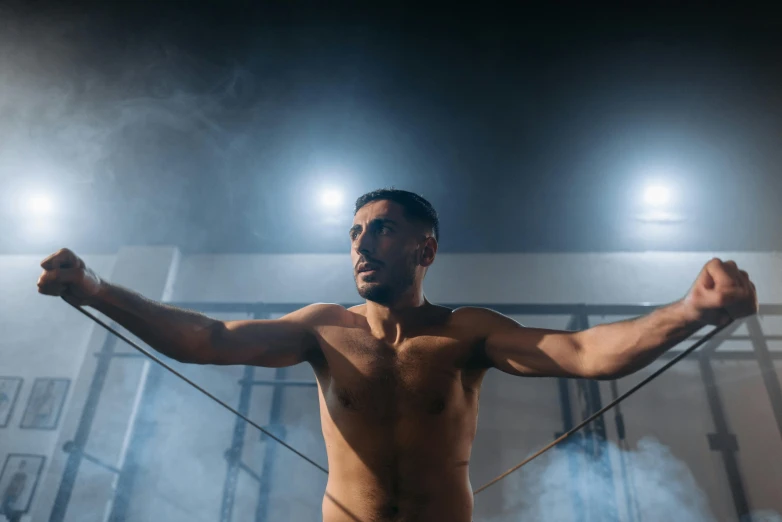 a shirtless man holding a rope in a gym, a portrait, pexels contest winner, background image, strong spotlights, featuring wires, bullet time