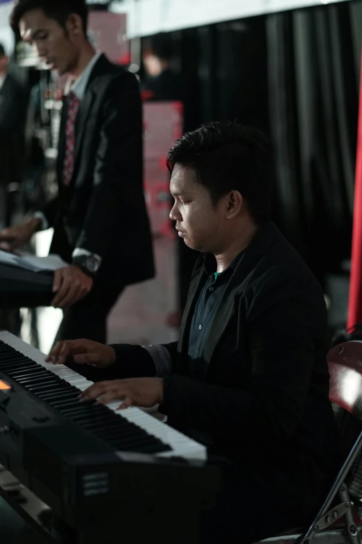 a group of people standing around a keyboard, by Basuki Abdullah, happening, attractive male playing piano, **cinematic, band, 15081959 21121991 01012000 4k