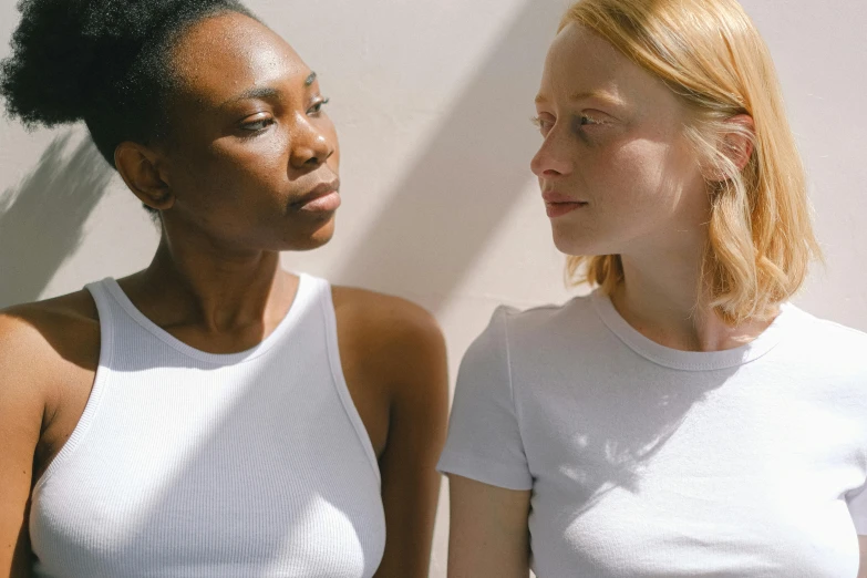 a couple of women standing next to each other, by Matija Jama, trending on pexels, renaissance, with a white complexion, dressed in a white t-shirt, dark people discussing, natural complexion