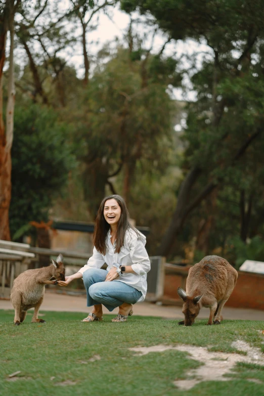 a woman kneeling on top of a lush green field, kangaroos, petting zoo, avatar image, smiling at camera