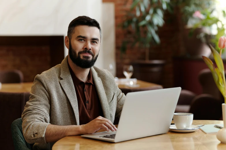 a man sitting at a table with a laptop, a portrait, trending on pexels, bearded, thumbnail, brown, hip corporate