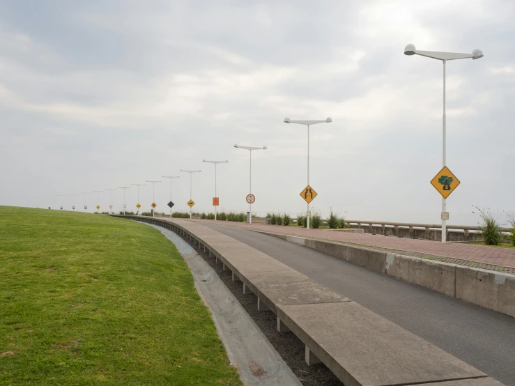 a group of street signs sitting on the side of a road, by Colijn de Coter, near the sea, street lighting, walkway, wide landscape