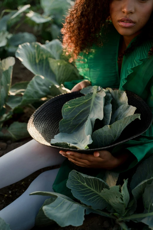 a woman sitting in a field holding a bowl of broccoli, by Jessie Algie, pexels contest winner, renaissance, black main color, big leaves, sustainable materials, vantablack gi