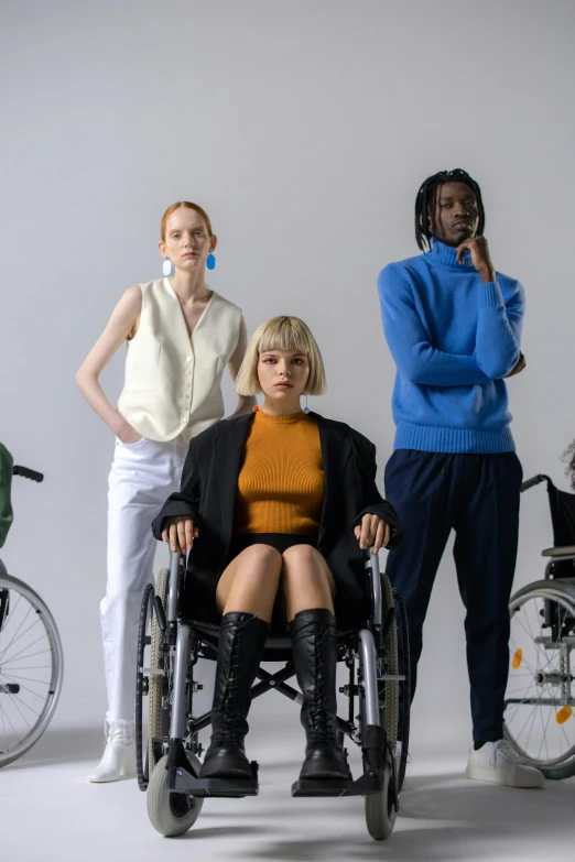 a group of people in wheelchairs posing for a picture, by Matija Jama, trending on unsplash, renaissance, fashion model features, in front of white back drop, wearing a turtleneck and jacket, colorful uniforms