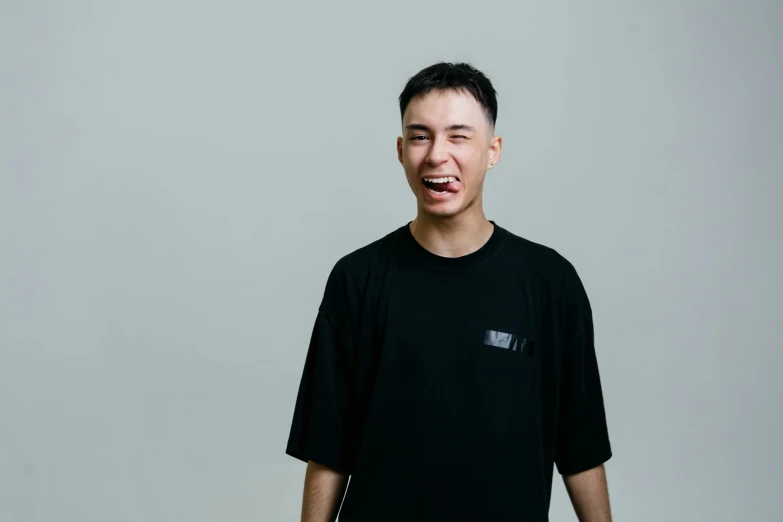 a man in a black shirt is making a funny face, an album cover, inspired by Tooth Wu, pexels contest winner, realism, young cute wan asian face, plain background, baggy, taken with sony alpha 9