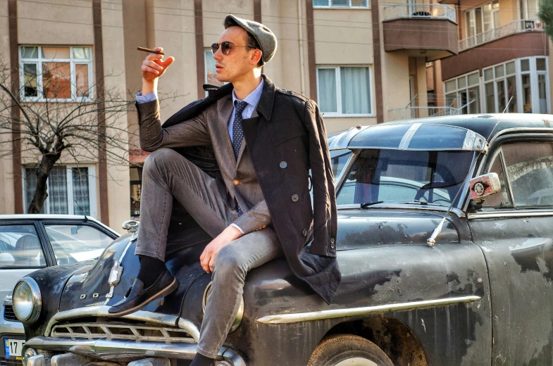 a man sitting on top of a car smoking a cigarette, by Niko Henrichon, pexels contest winner, photorealism, trench coat and suit, with a cool pose, orthodox, instagram model