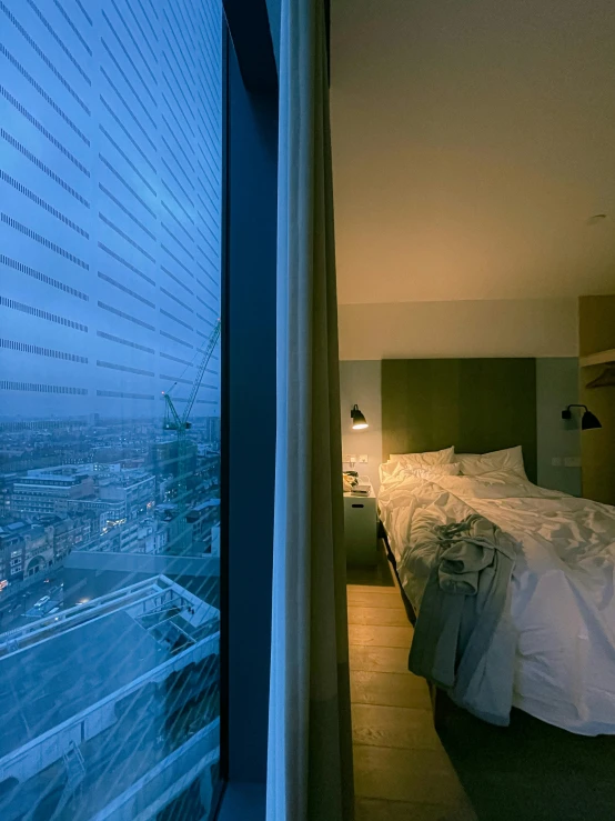 a bed sitting in a bedroom next to a window, the shard, 4 k cinematic panoramic view, 2 4 mm iso 8 0 0, warsaw