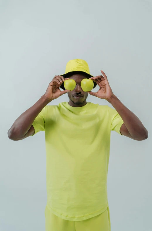 a man holding tennis balls in front of his face, pexels contest winner, tyler the creator, plain background, wearing hi vis clothing, ( ( dark skin ) )