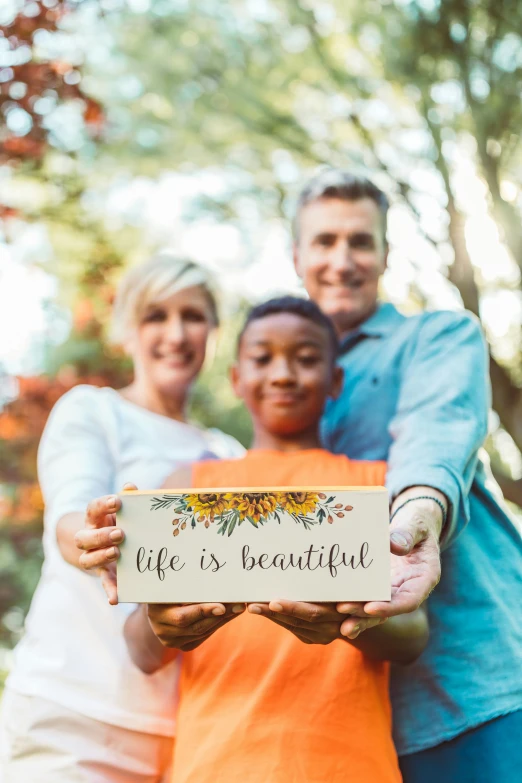 a family holding a sign that says life is beautiful, pexels contest winner, autumn tranquility, holding gift, colored photo, beautiful skin