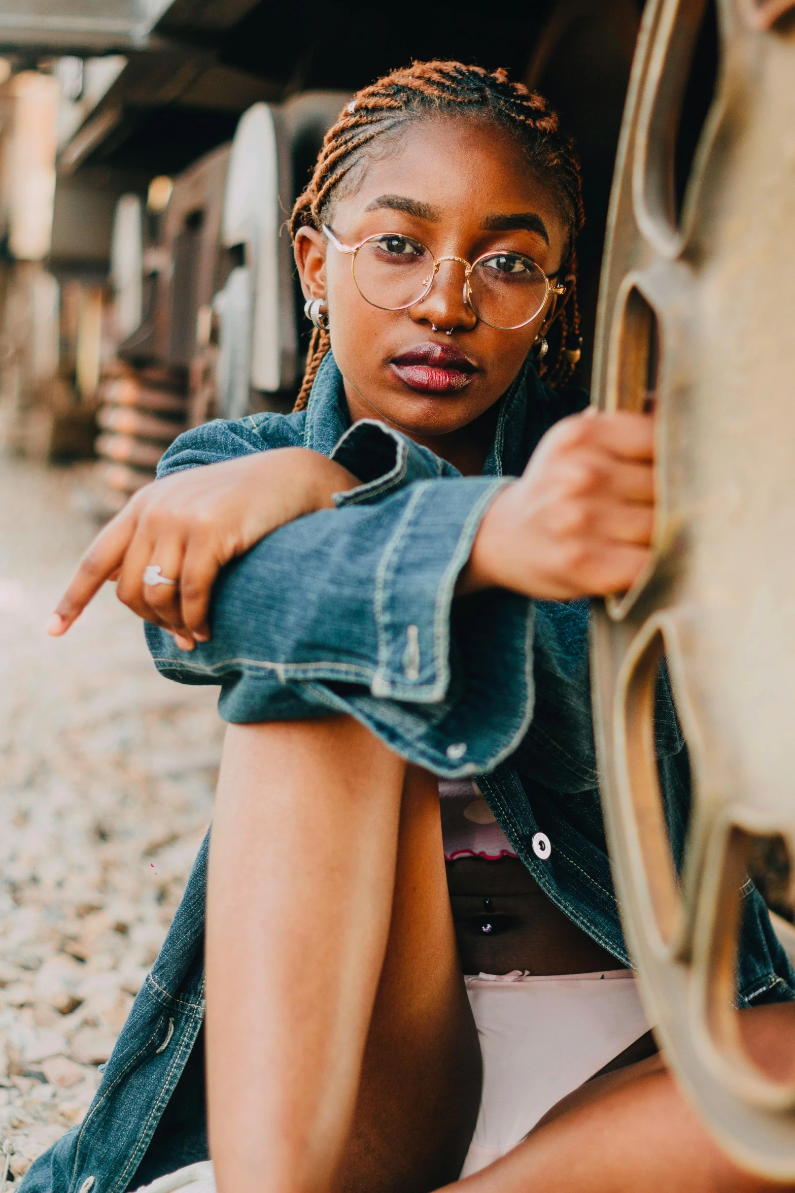 a woman sitting on the ground next to a train, trending on pexels, portrait willow smith, square rimmed glasses, jean jacket, full frame image