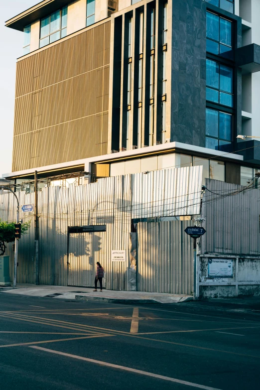 a man riding a skateboard down a street next to a tall building, an album cover, unsplash, thailand, industrial architecture, dwell, seen from a distance