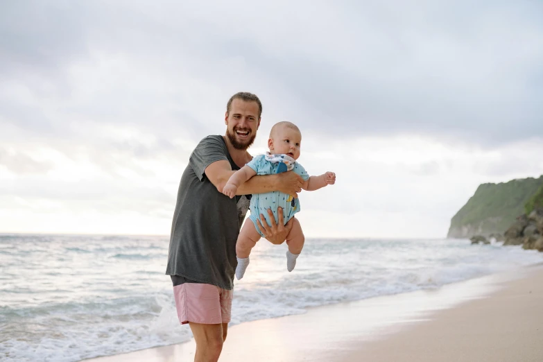 a man holding a baby on a beach, pexels contest winner, happening, avatar image, australian beach, happy people, kauai