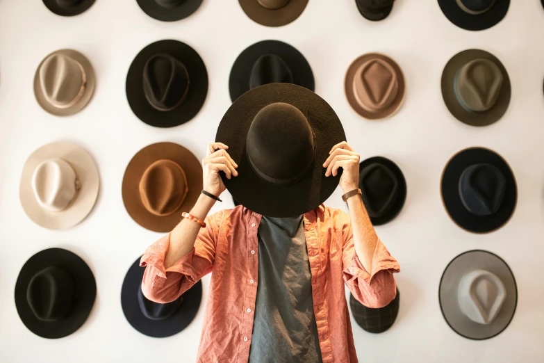 a man standing in front of a wall of hats, trending on pexels, heath clifford, thumbnail, woman, flat lay