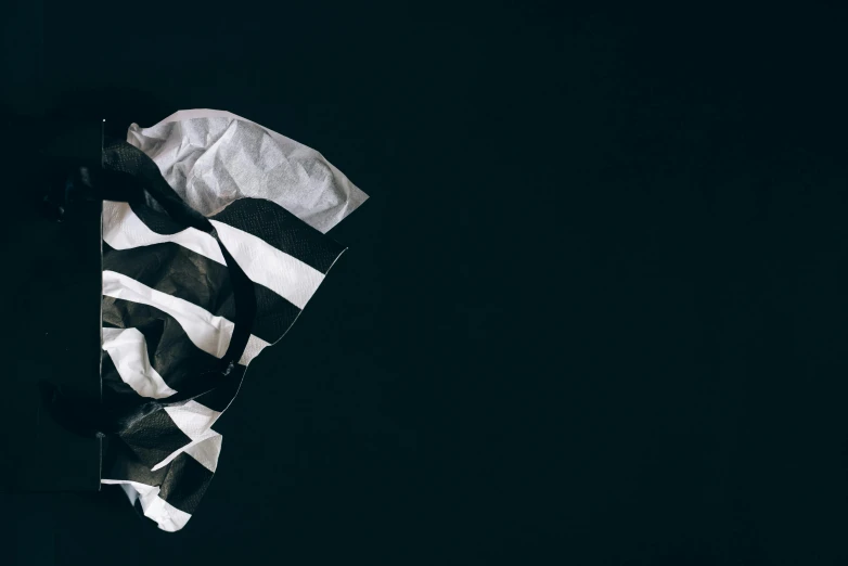 a black and white flag laying on top of a table, inspired by Anna Füssli, unsplash contest winner, black backdrop, prisoner, paper crumpled texture, striped