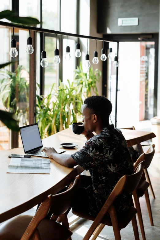 a man sitting at a table with a laptop, pexels contest winner, big windows, african canadian, open plan, lush surroundings