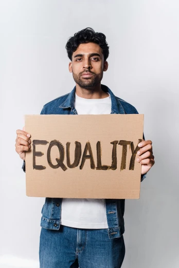 a man holding a sign that says equality, an album cover, trending on pexels, renaissance, indian, handsome, studio photo, brown