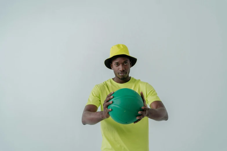 a man in a yellow shirt holding a green ball, inspired by Paul Georges, pexels contest winner, bucket hat, ( ( dark skin ) ), various posed, without text
