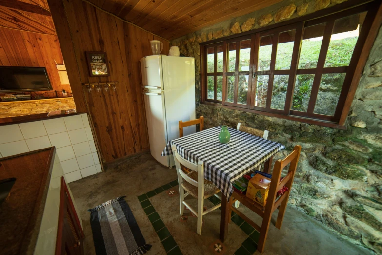 a kitchen with a table and a refrigerator, by Felipe Seade, unsplash, light inside the hut, gradins view, slide show, lush surroundings