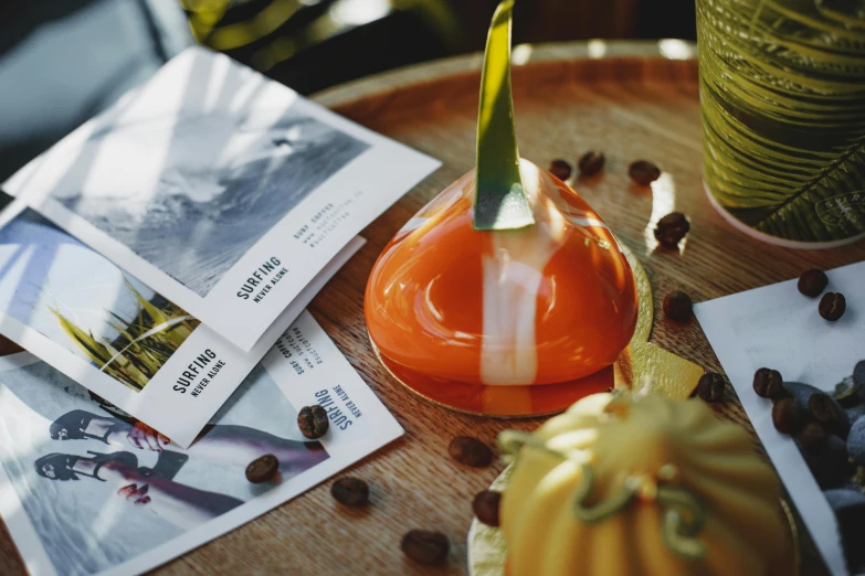 an orange vase sitting on top of a wooden table, inspired by Charles Le Roux, unsplash, private press, glass domes, latte art, pair of keycards on table, tropical mood