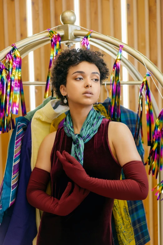 a woman standing in front of a rack of clothes, trending on pexels, renaissance, wearing a scarf, jewel tones, mixed-race woman, at a fashion shoot