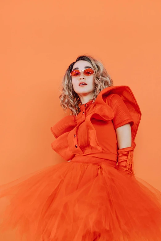 a woman in an orange dress and sunglasses, an album cover, by Winona Nelson, trending on pexels, saoirse ronan, * colour splash *, holding a pudica pose, poofy