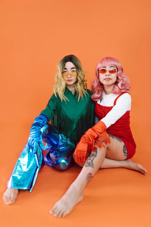 two women sitting next to each other on an orange background, an album cover, inspired by Wang Duo, trending on pexels, pop art, cosplayer dressed like a crab, holographic suit, orange hair, cosplay photo