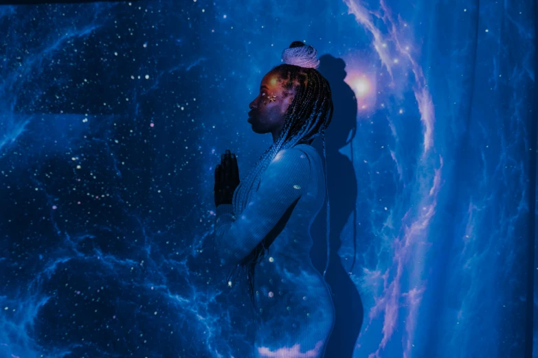 a man with dreadlocks standing in front of a galaxy, an album cover, by Julia Pishtar, pexels contest winner, afrofuturism, praying meditating, black young woman, blue bioluminescence, god is a girl