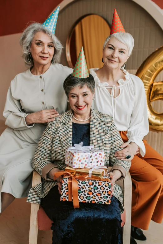 two women sitting next to each other holding a birthday cake, pexels contest winner, modernism, wearing a grey wizard hat, three women, tight wrinkled cloath, birthday wrapped presents